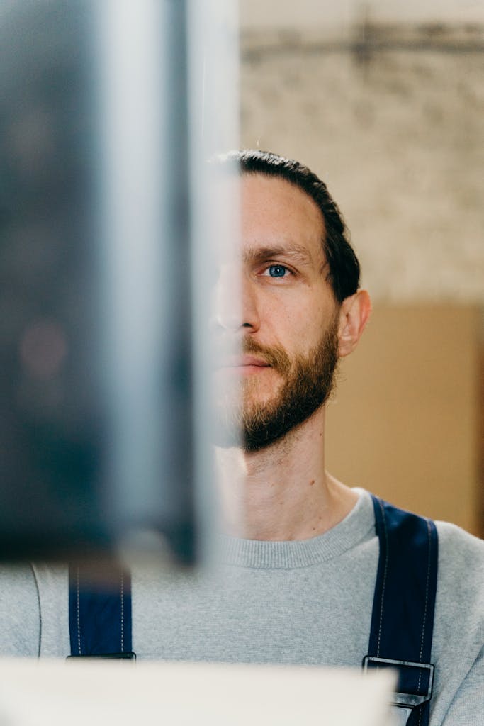 Close-up portrait of a bearded man with blue eyes in casual attire, partially obscured view.